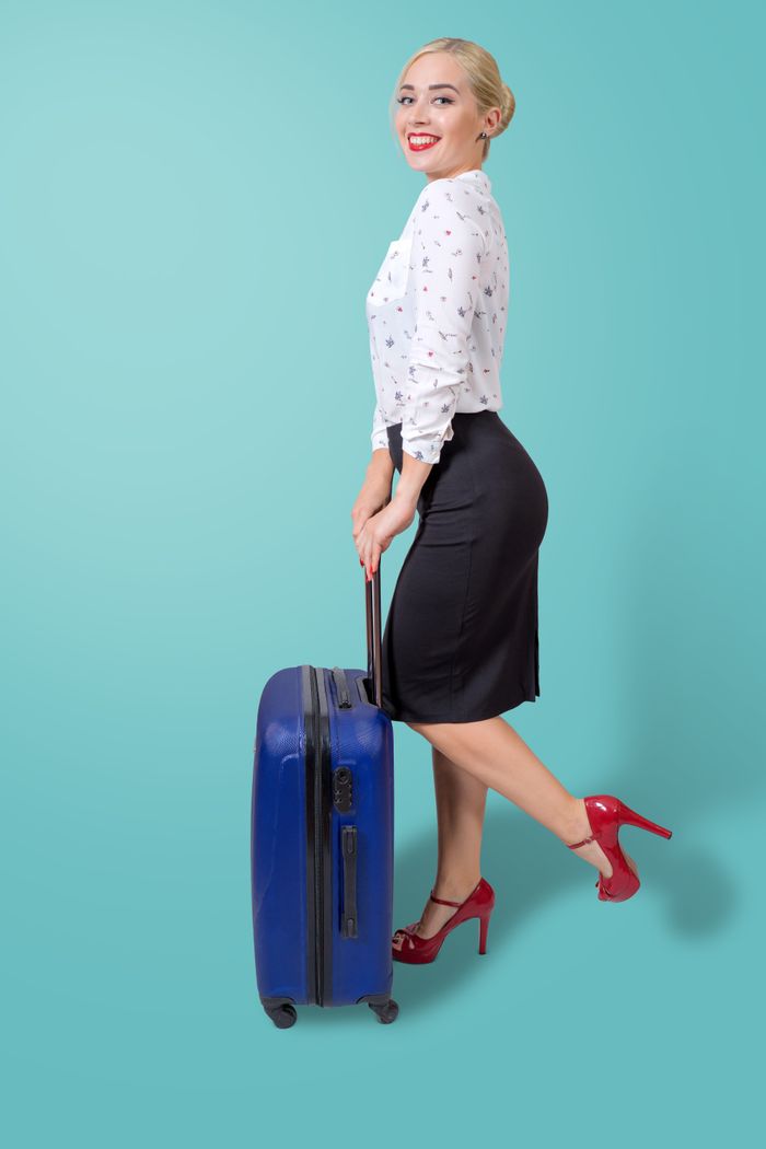 The Art of Drawing Readers In: Your attractive post title goes here Smiling woman in a business outfit holding luggage against a blue background.